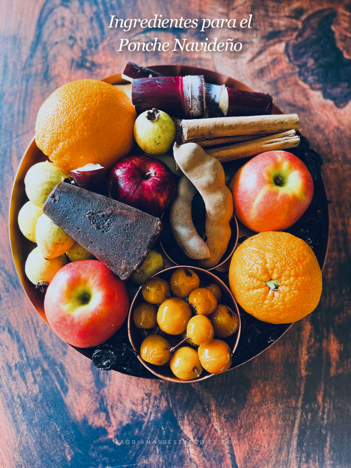 un plato de madera con frutas de temporada como naranja, manzanas, tejocotes mexicanos, guayabas.