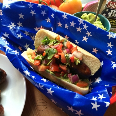 Firecracker Pork Brats garnished with pico de gallo and avocado to add a latin twist to a traditional American dish