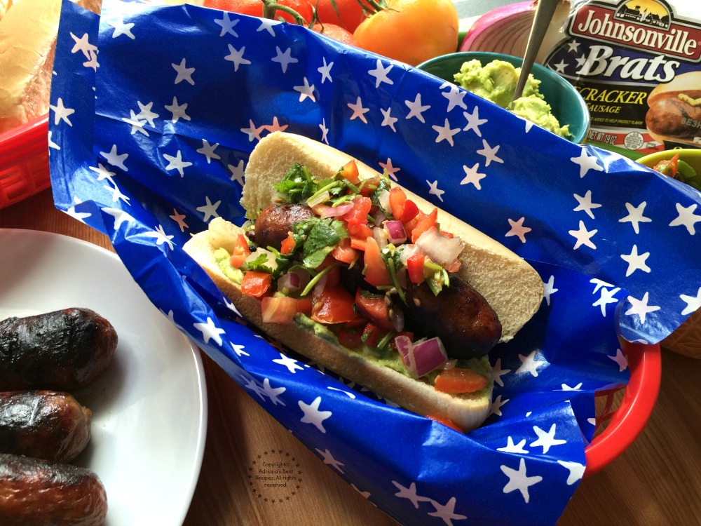 Firecracker Pork Brats garnished with pico de gallo and avocado to add a latin twist to a traditional American dish