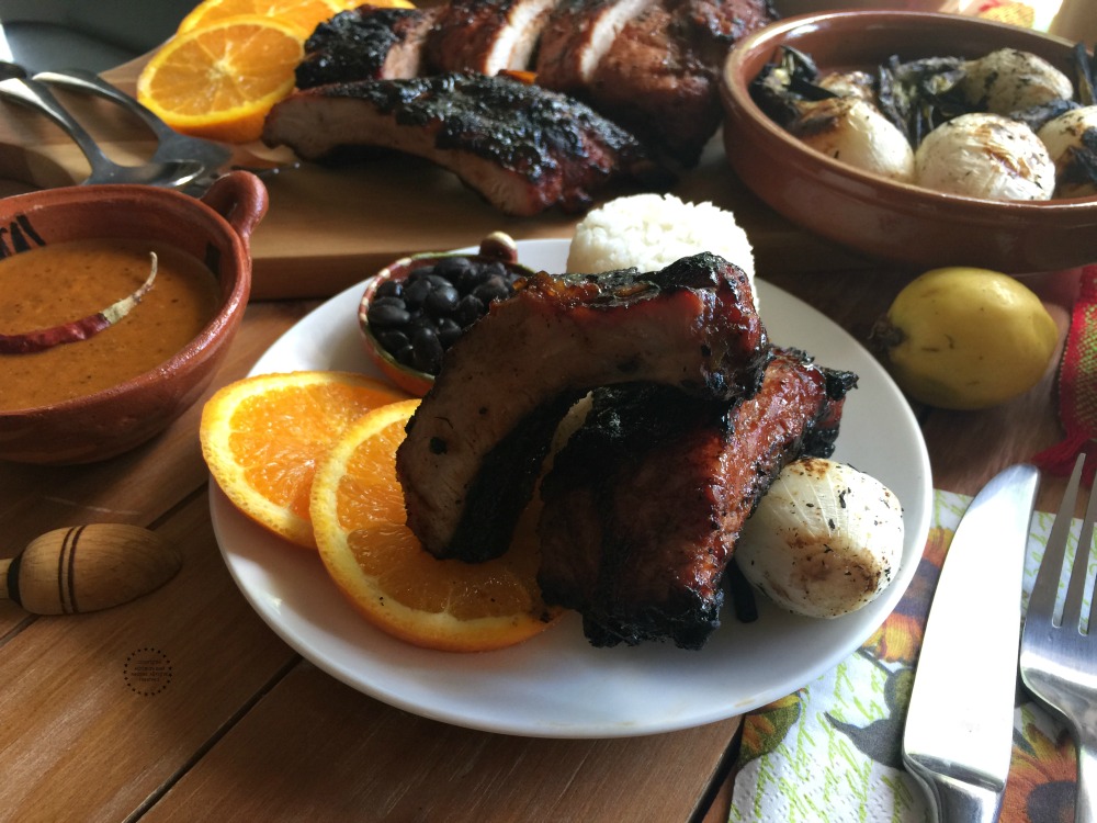 A plate of chipotle guava BBQ pork back ribs with rice, beans and orange slices