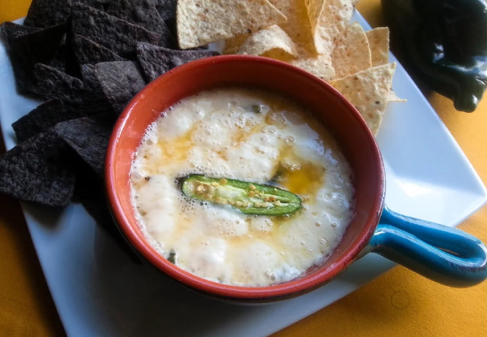 The recipe for the queso fundido has shredded cheese, and poblano peppers. Serving with corn chips for a tasty appetizer.