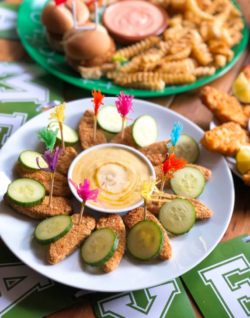 Estas son los Gardein Seven-Grain Crispy tenders acompañados con una salsa vegana de mostaza y miel casera. Servido con divertidas banderillas coloridas y rodajas de pepino. 