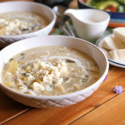 Caldillo de queso fresco con papas servido en un tazón y adornado con más queso fresco y cintas de crema fresca Mexicana