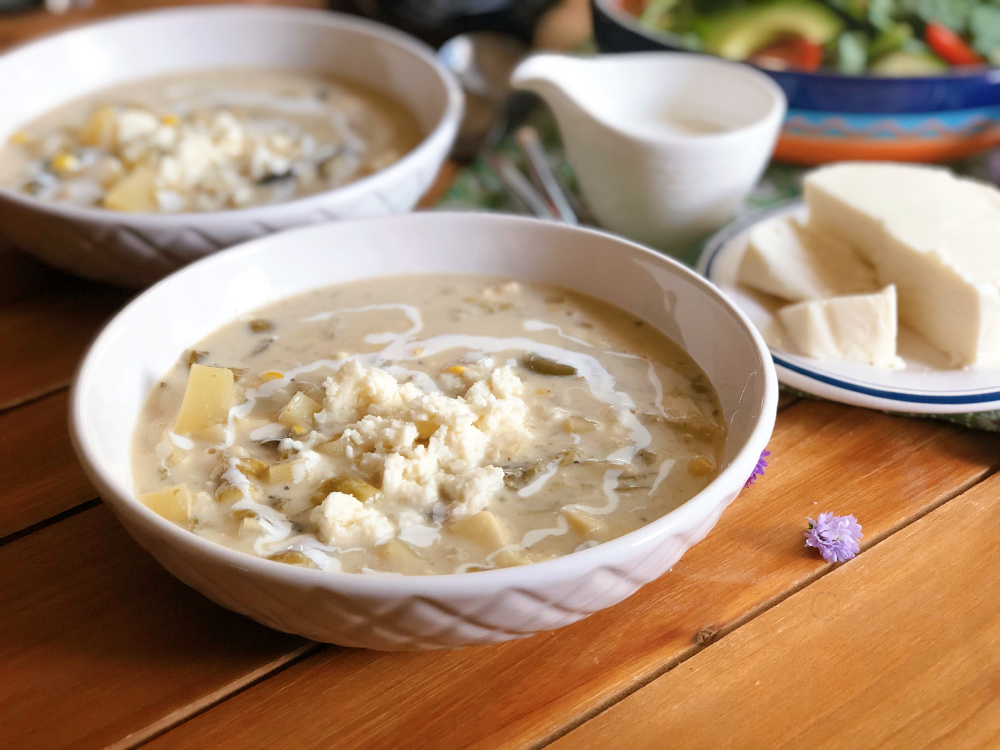 Caldillo de queso fresco con papas servido en un tazón y adornado con más queso fresco y cintas de crema fresca Mexicana