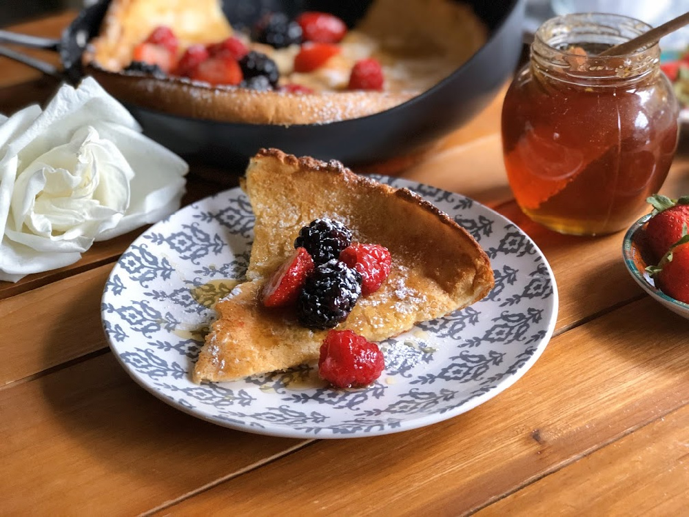 Dutch baby pancakes garnished with berries, honey, and confectioners sugar.