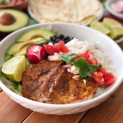 The Chipotle Pork Chops Bowl has grilled boneless pork chops, white rice, black beans, lettuce, avocado slices, radishes, and pico de gallo.