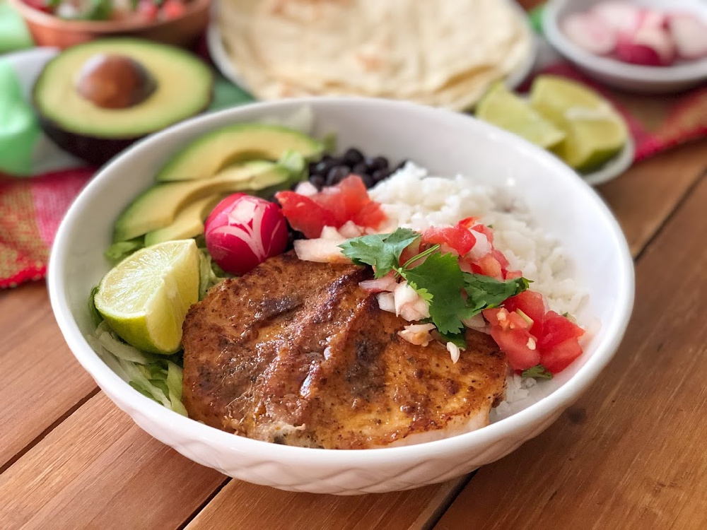 The Chipotle Pork Chops Bowl has grilled boneless pork chops, white rice, black beans, lettuce, avocado slices, radishes, and pico de gallo.