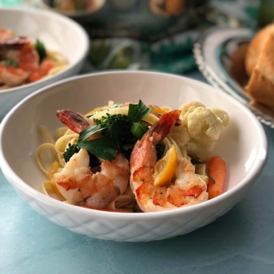 A white bowl with shrimp primavera and colorful veggies garnished with parsley and preserved lemons