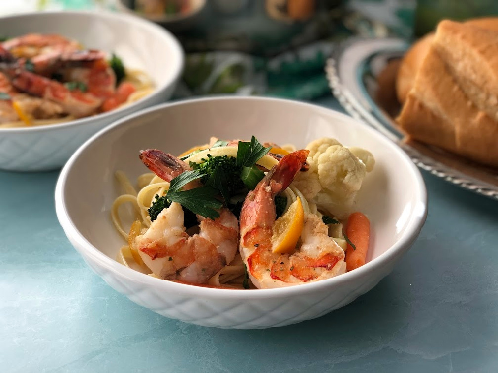 A white bowl with shrimp primavera and colorful veggies garnished with parsley and preserved lemons