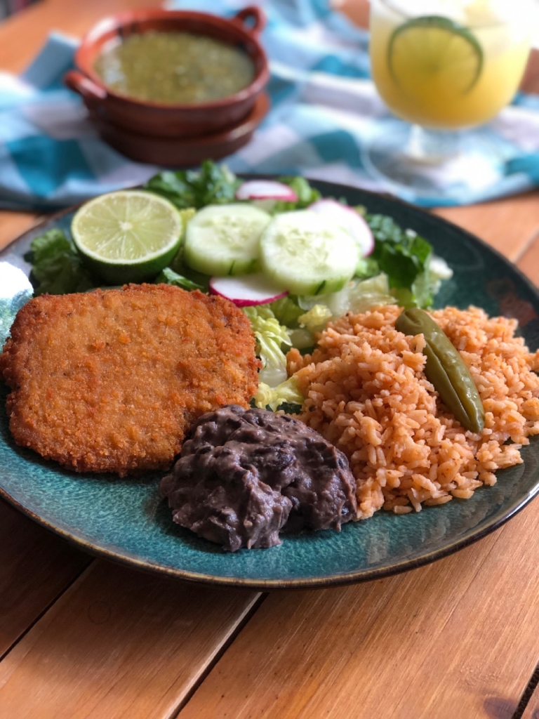 Esta es el platillo de milanesa de cerdo servida con una ensalada verde, arroz mexicano y una guarnición de frijoles negros refritos.