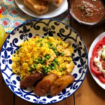 Arroz con Pollo a la Cubana servido con plátanos fritos, una ensalada de tomate, y pan caliente