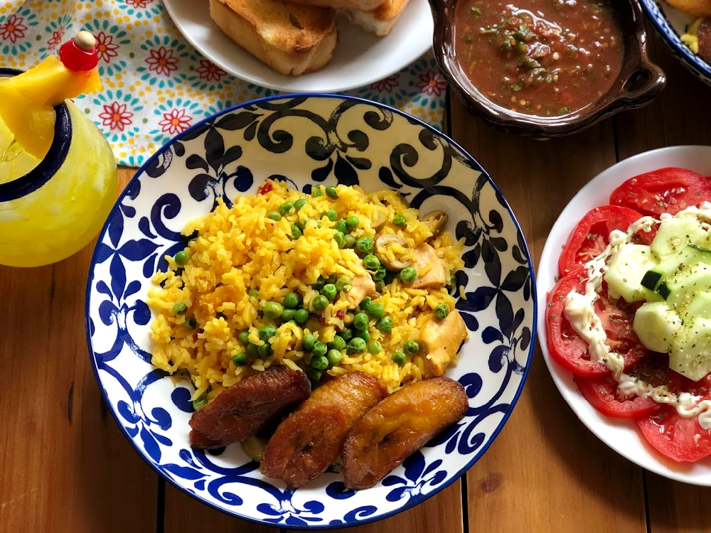 Arroz con Pollo a la Cubana servido con plátanos fritos, una ensalada de tomate, y pan caliente