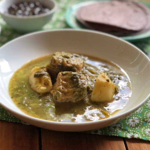 Un tazón blanco con cerdo con verdolaga en salsa de tomatillo