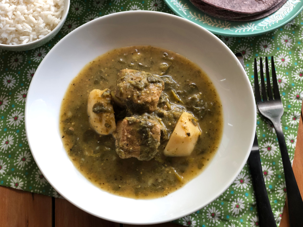 Un tazón con guisado de cerdo con verdolagas, salsa verde casera y papas