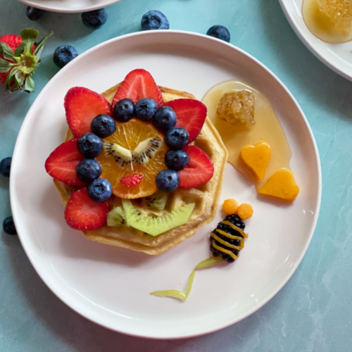 a white plate with breakfast waffles with a happy flower made with fruits