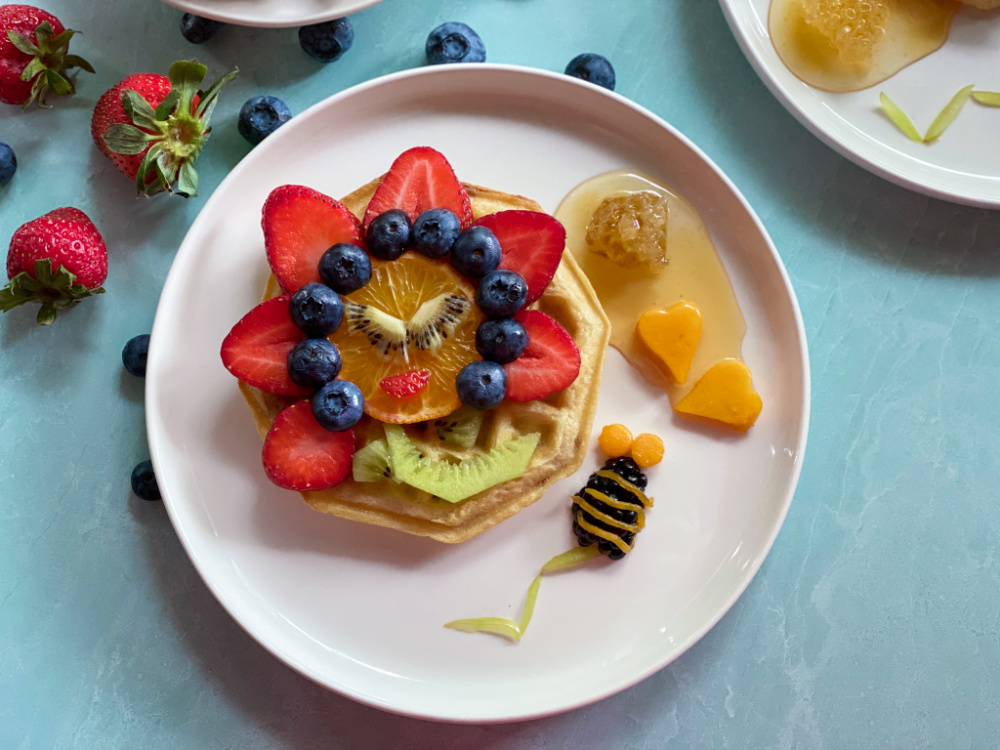 a white plate with breakfast waffles with a happy flower made with fruits