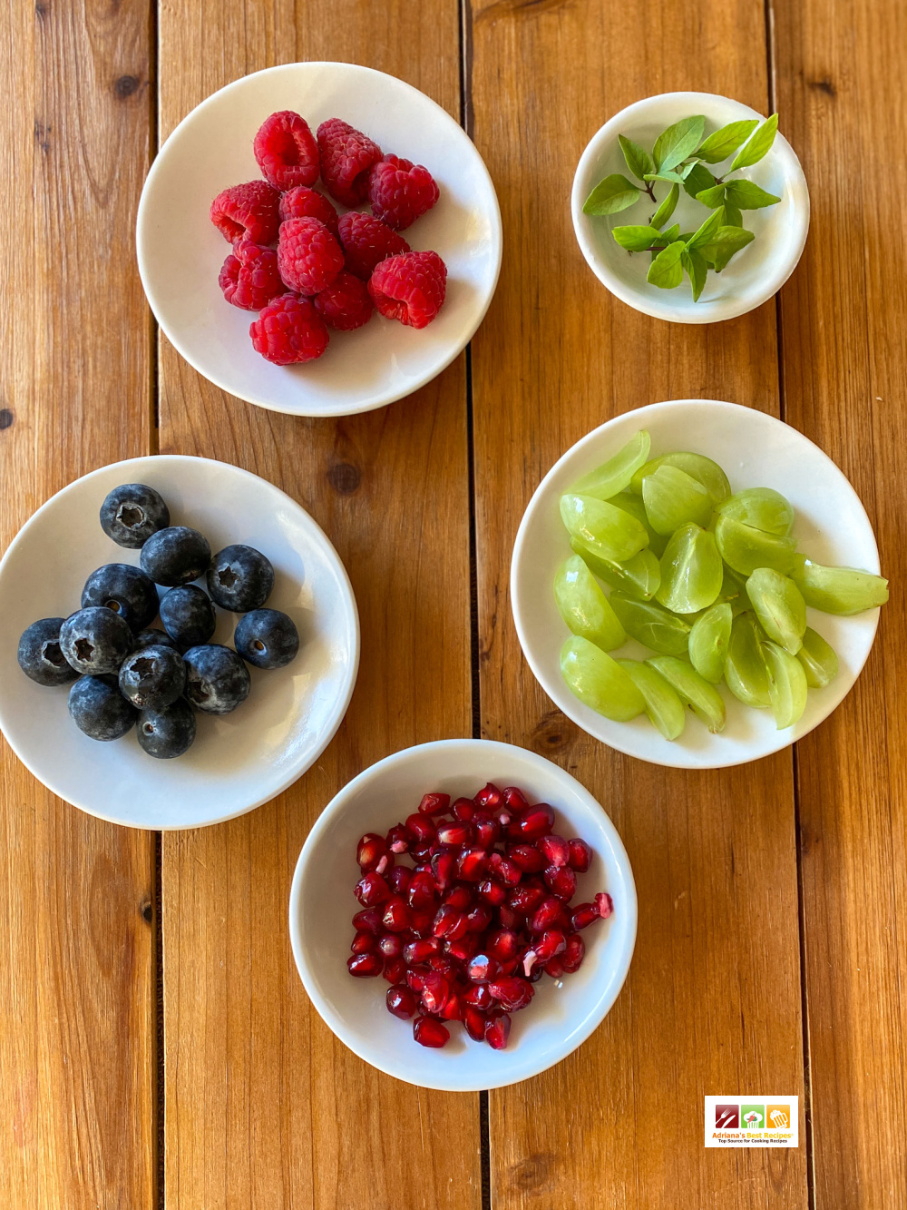 Small plates with berries, grapes, pomegranate seeds, and lemon basil