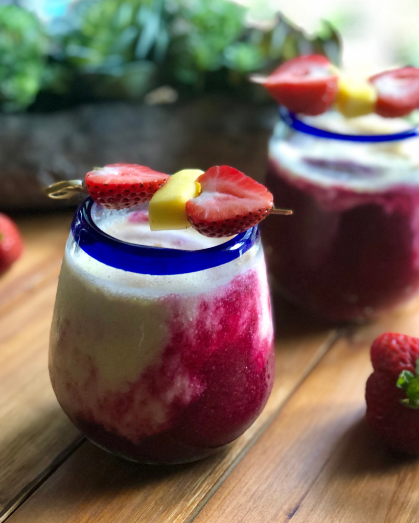 Two glasses served with a layered mango strawberry beet power smoothie