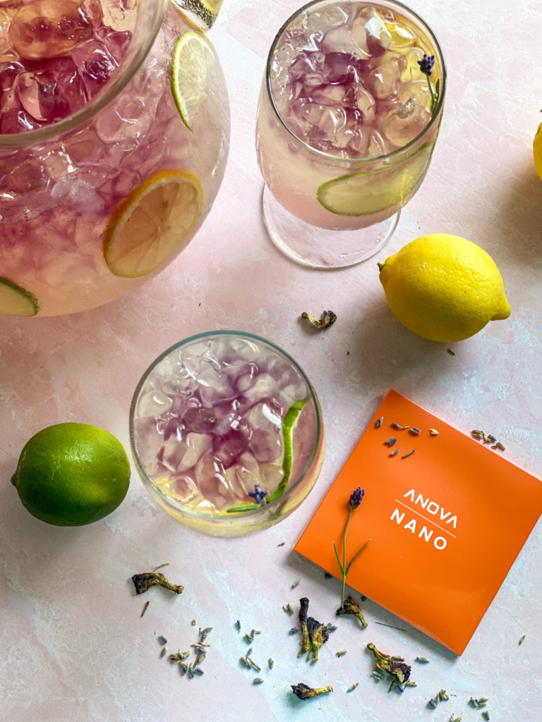 A pitcher and two glasses with lavender lemonade and lemon rounds