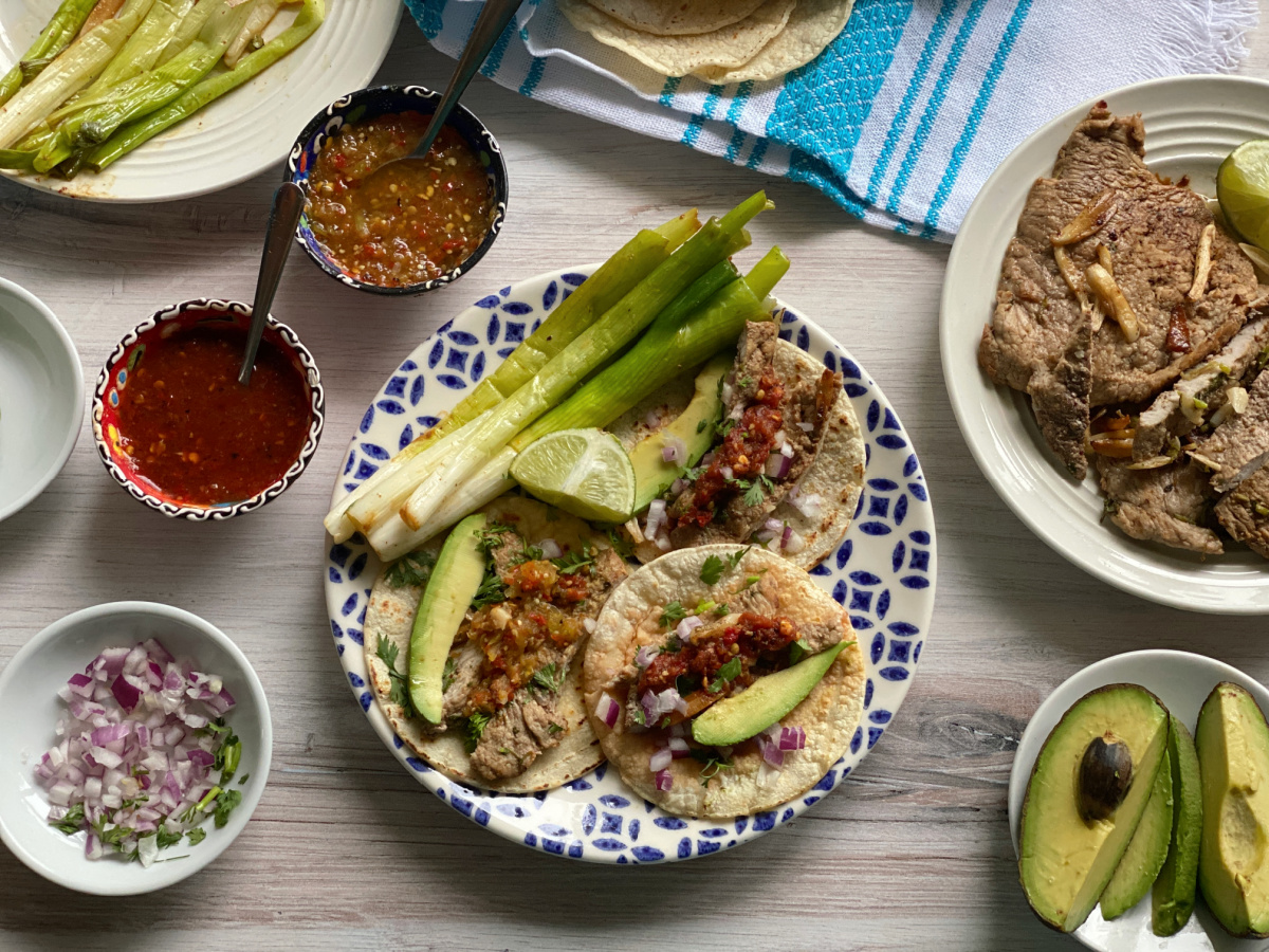 Una foto superior que muestra un plato con tacos servidos con cebollas y rodajas de aguacate.