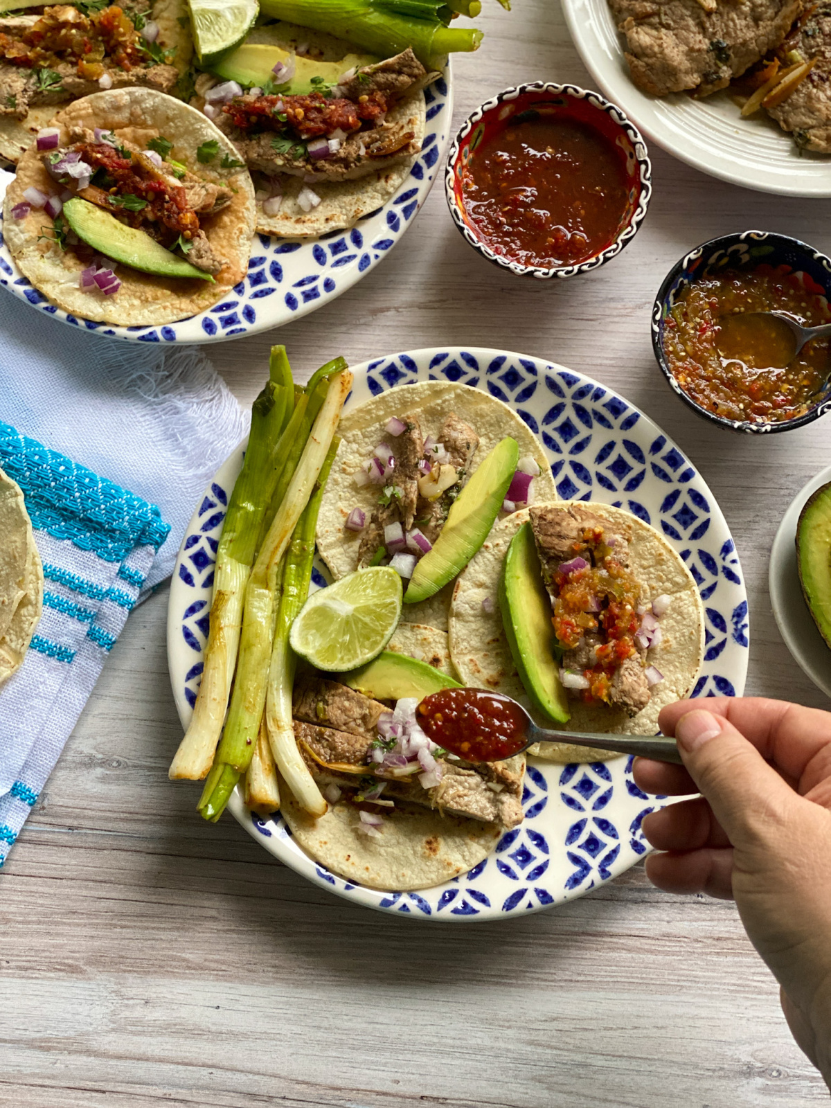 A hand garnishing tacos with taquera salsa