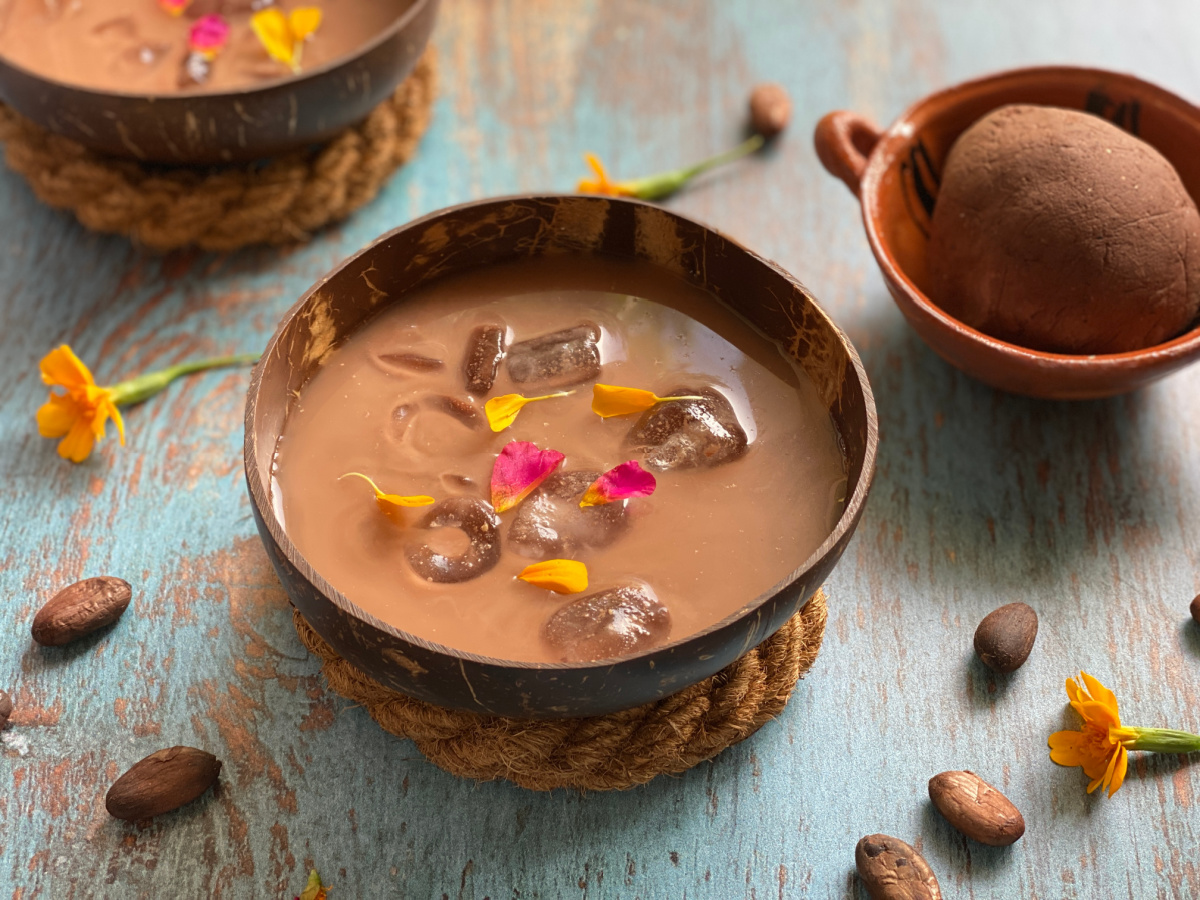 Una jicarita con hielo y una bebida de maíz y granos de cacao