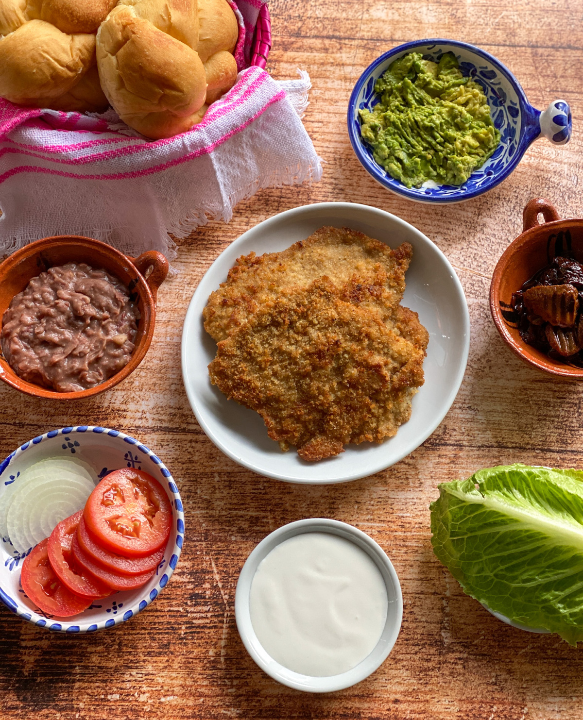 Components for the veal milanesa torta include breaded veal, refried beans, tomato, onion, lettuce and more