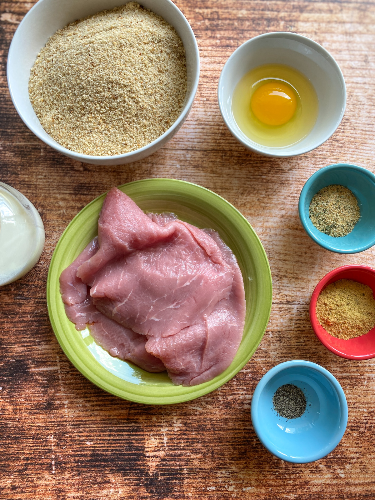 Los ingredientes para la milanesa de ternera incluyen pan molido, huevos, condimentos y filetes de ternera.