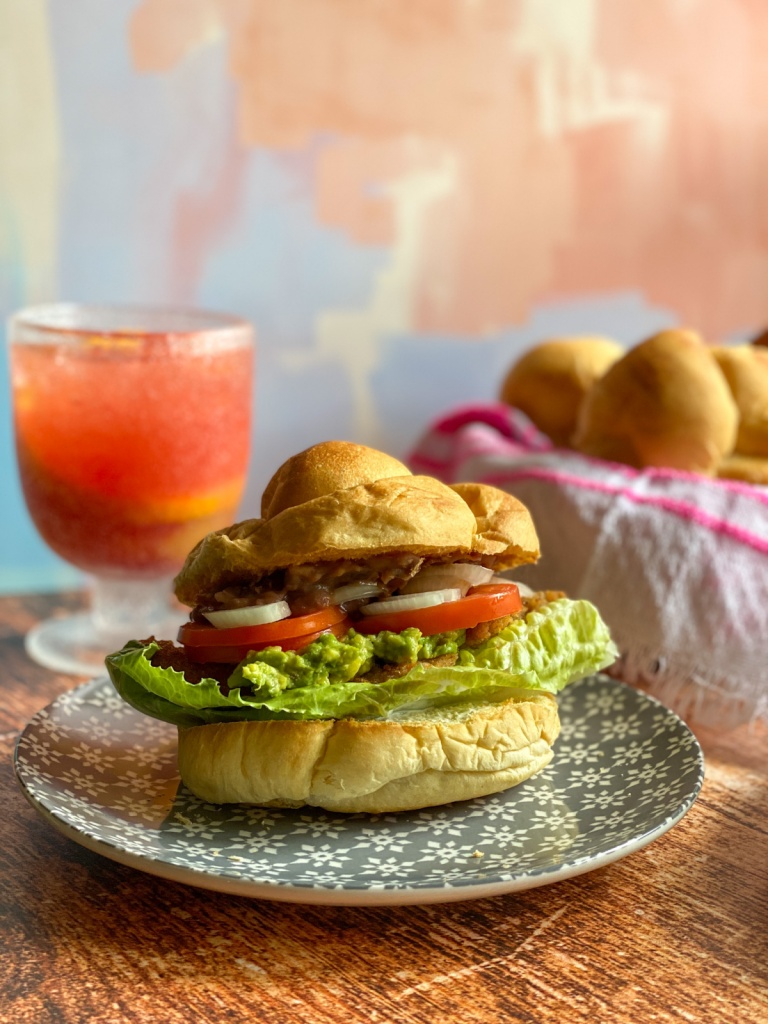Este es el sándwich de ternera milanesa al estilo mexicano servido en un plato acompañado con jugo de arándano con naranja