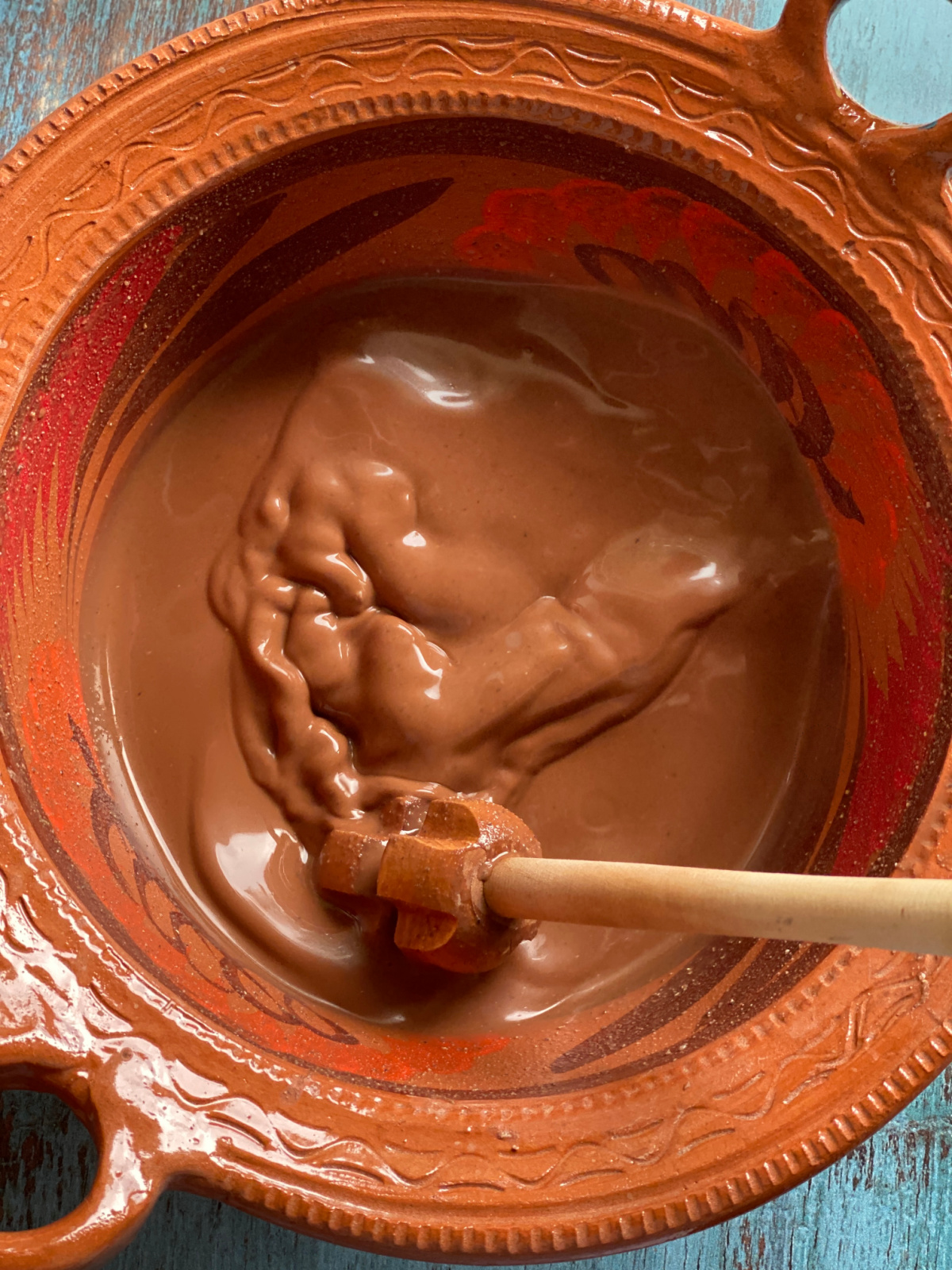 batiendo una mezcla de maíz y cacao dentro de una olla de barro y un molinillo de madera