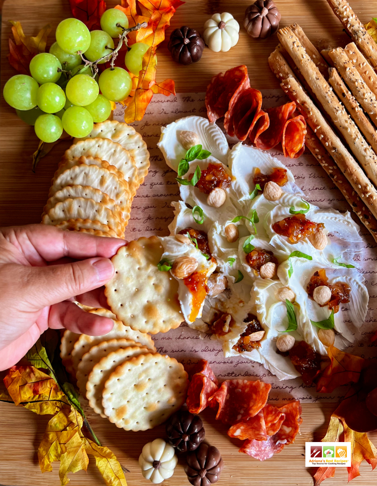 una mano sosteniendo una galleta con queso batido, chutney y almendras