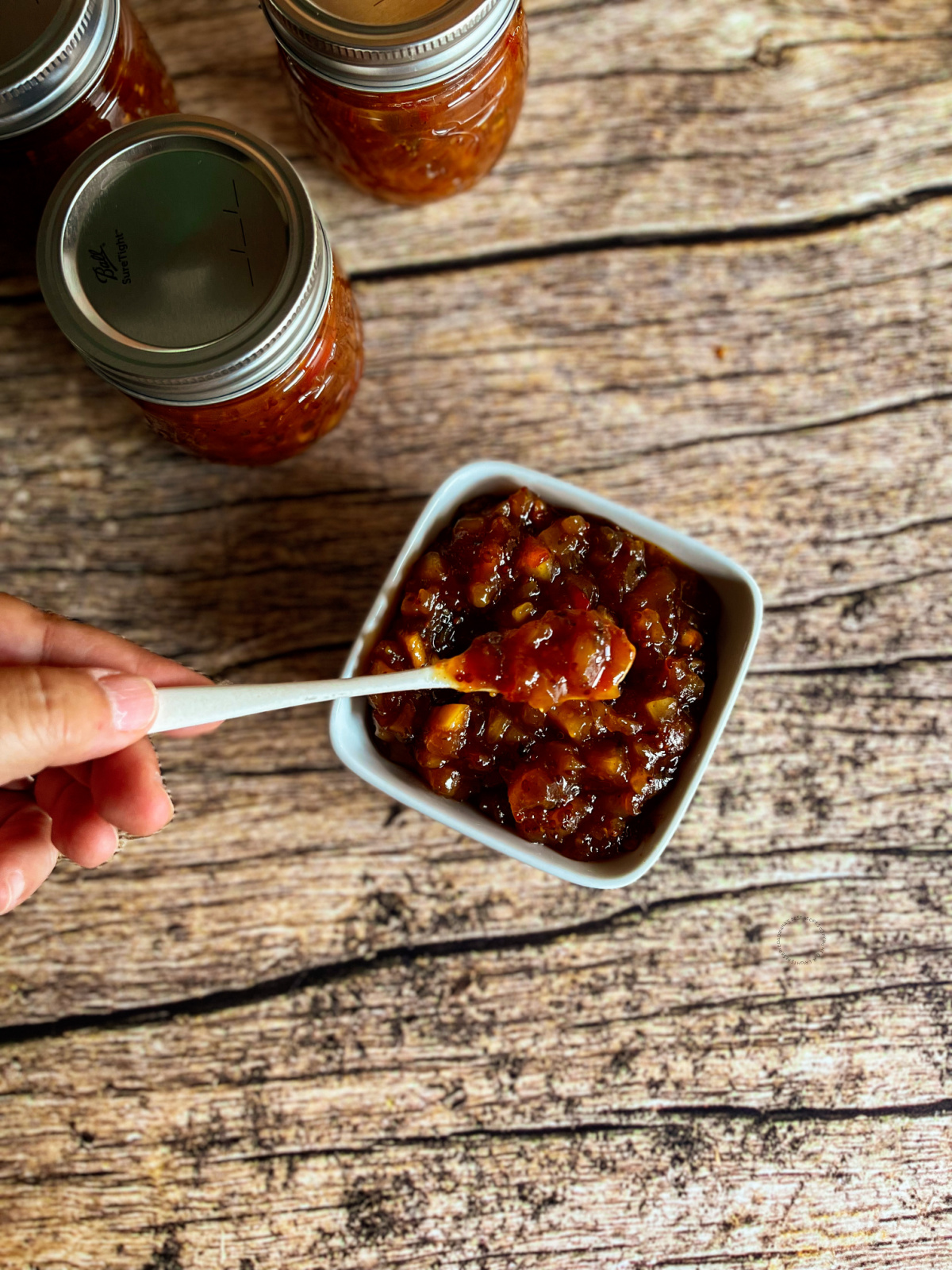 a hand holding a spoonful of chutney ready for a butter board